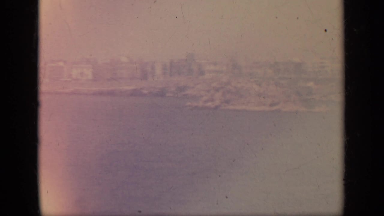 1963 8mm Greece footage showing a hazy coastal town or shoreline seen from the sea, with faded color and film wear.