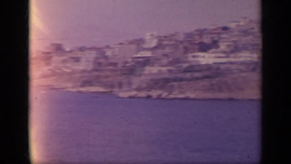 1963 8mm Greece view of a dense hillside coastal town overlooking blue sea, filmed from a moving boat.