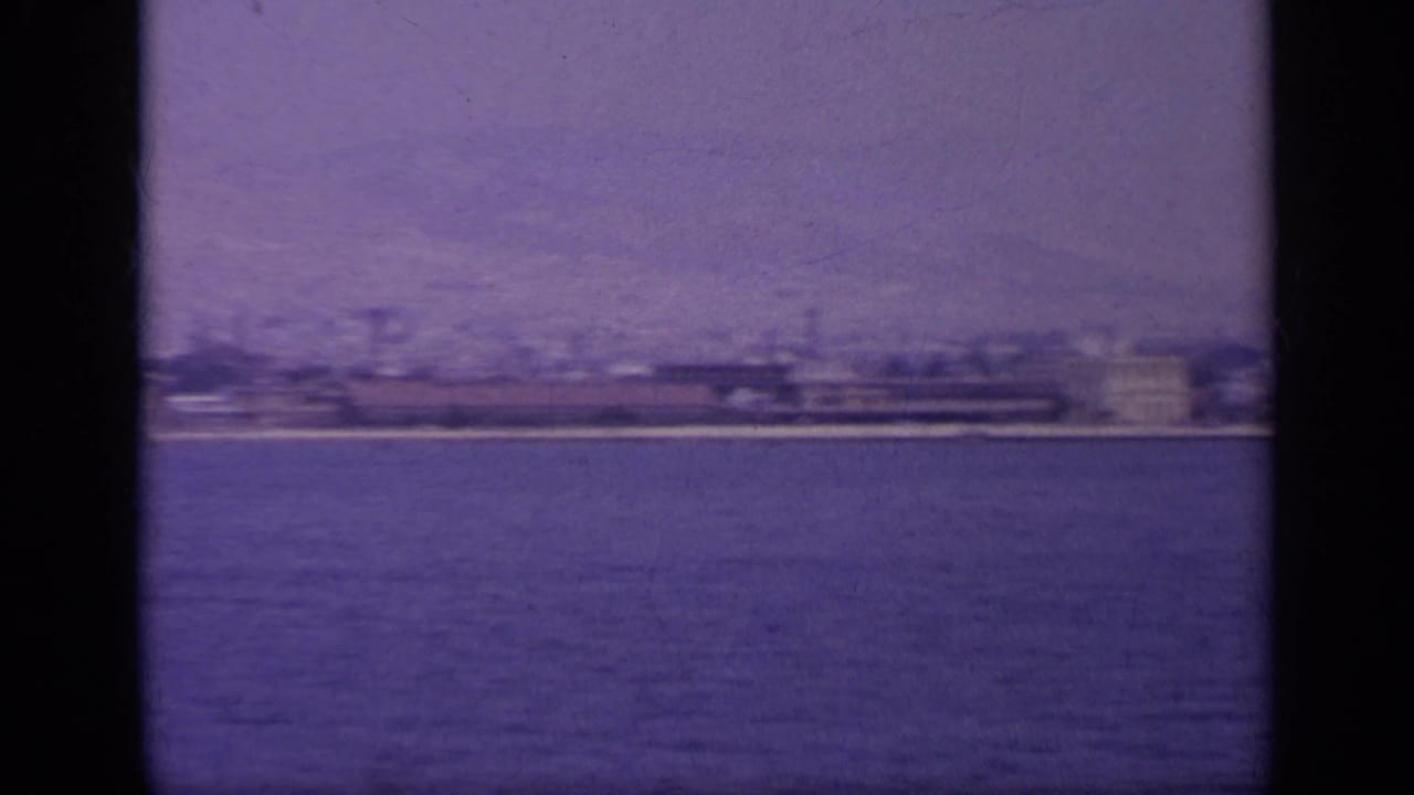 1963 Greece waterside view of a more industrial shoreline with long low structures and possible smokestacks across the water.