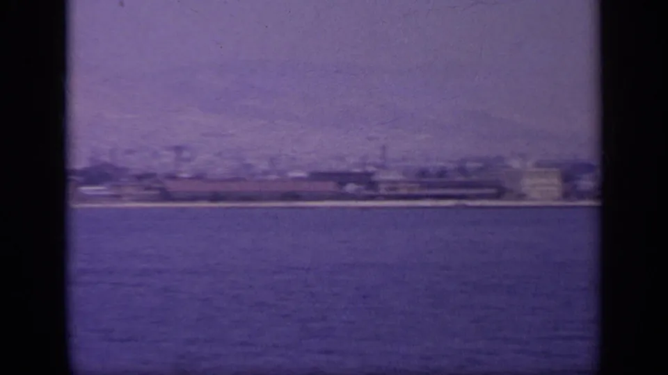 1963 Greece waterside view of a more industrial shoreline with long low structures and possible smokestacks across the water.