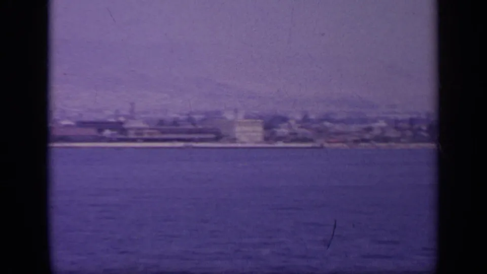 1963 Greece home-movie frame showing a hazy coastal city seen from a moving boat across open water.