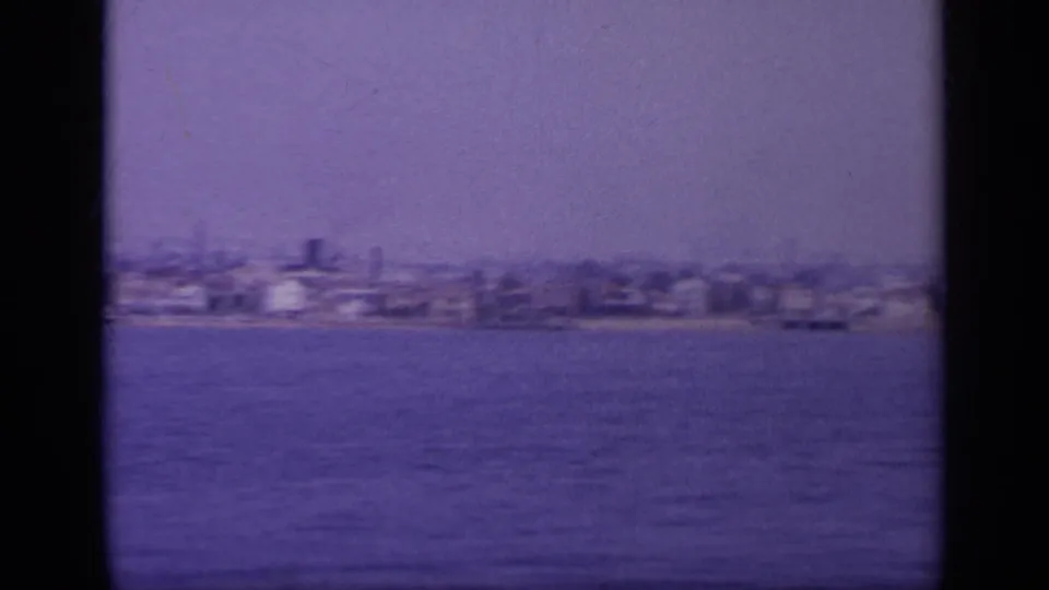 Aged 8mm frame of a Greek shoreline in 1963, with scattered waterfront structures seen from offshore.