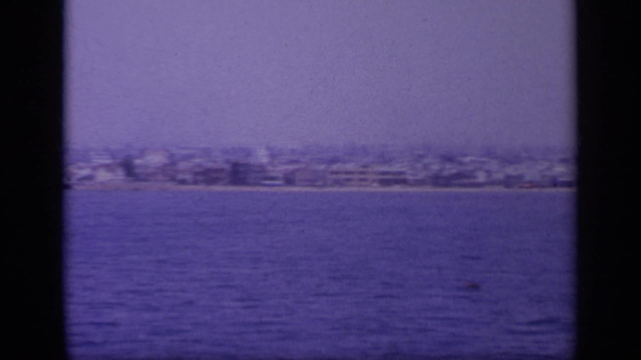 Final 1963 Greece boat-view frame showing a distant coastal city, open water, and strong aged-film coloration.