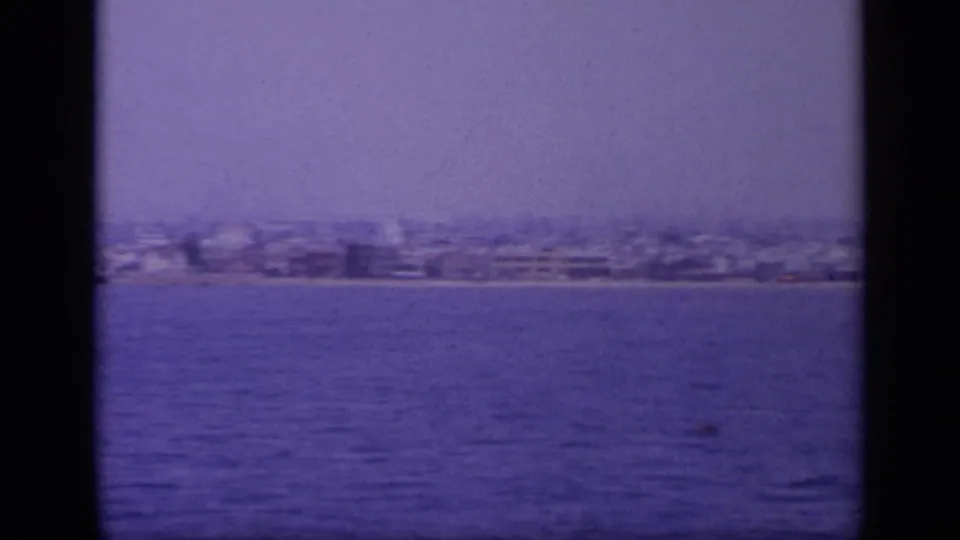 Final 1963 Greece boat-view frame showing a distant coastal city, open water, and strong aged-film coloration.
