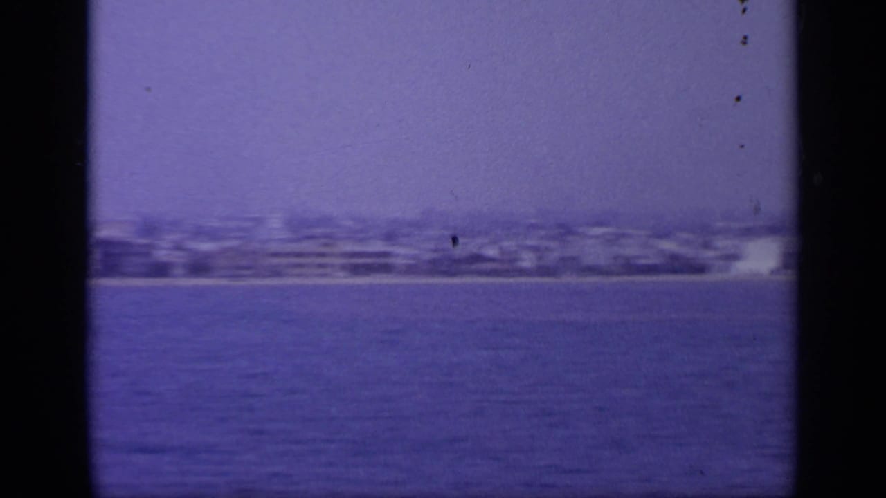 Distant shoreline and city buildings across blue water with dark film edges.
