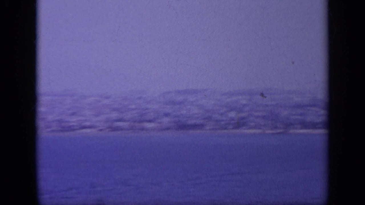 Hazy shoreline and low hills seen across blue water.