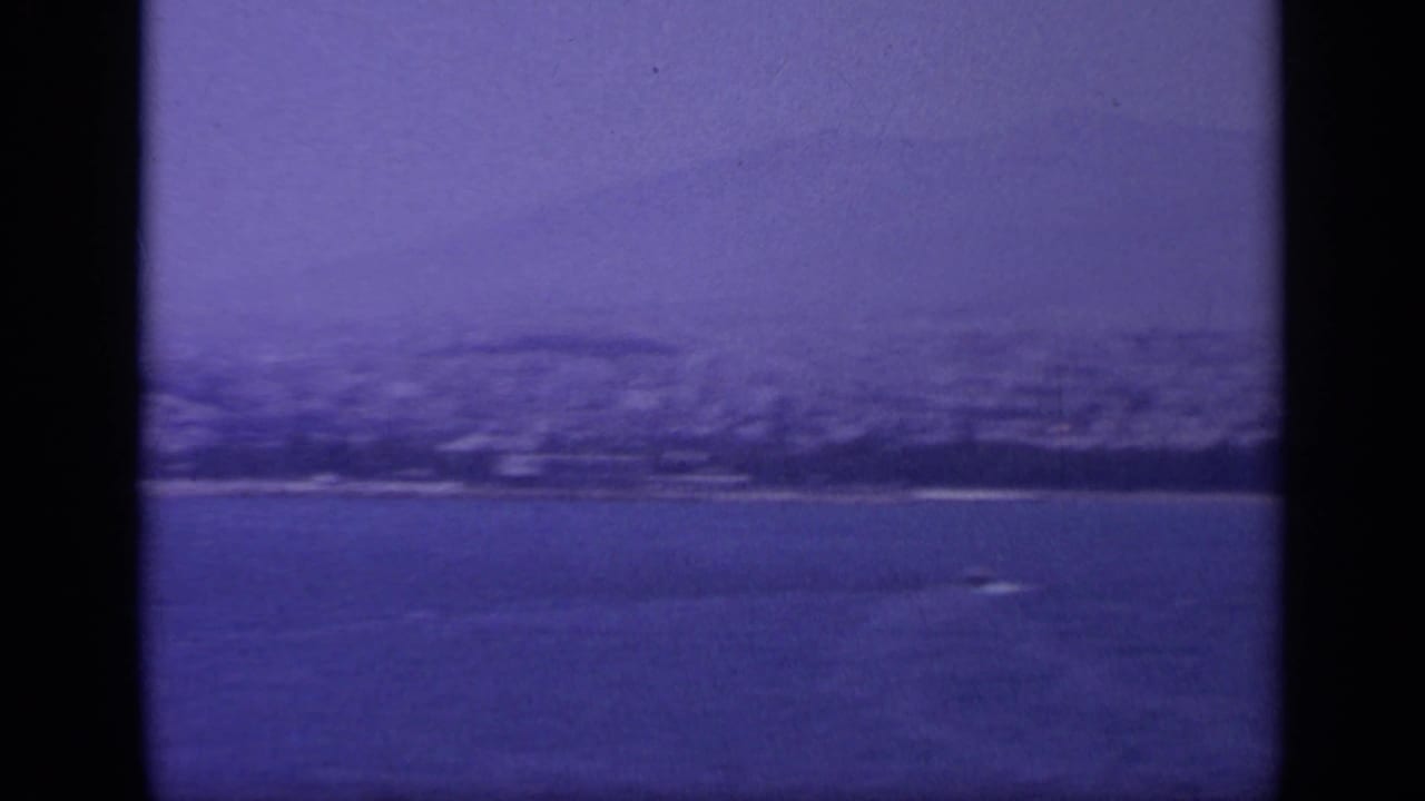 Aged 8mm frame of a Greek rocky coastline, with open water in front and shadowed hills softened by blue color shift.