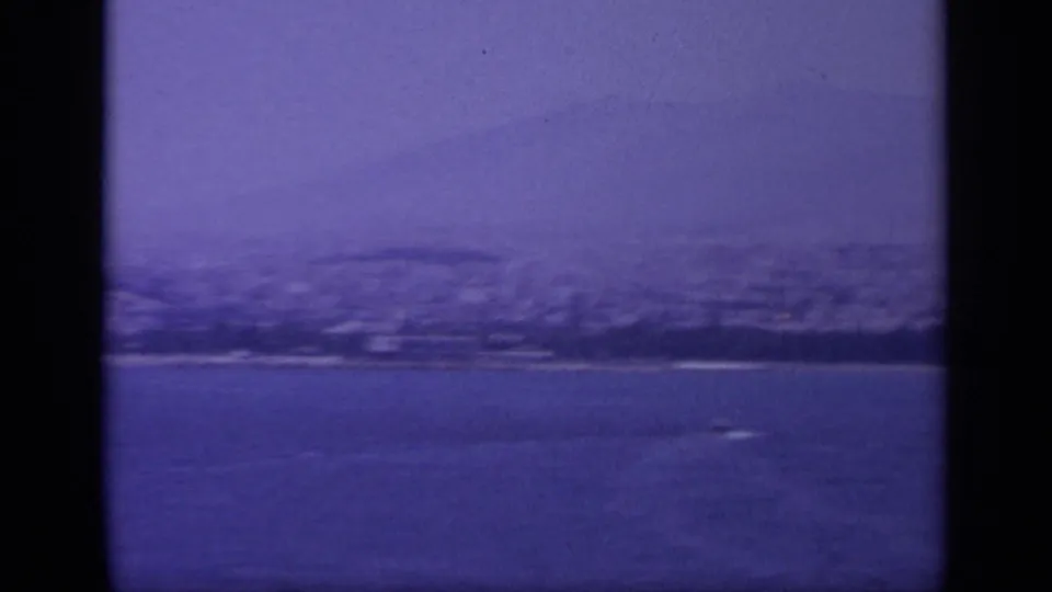 Aged 8mm frame of a Greek rocky coastline, with open water in front and shadowed hills softened by blue color shift.