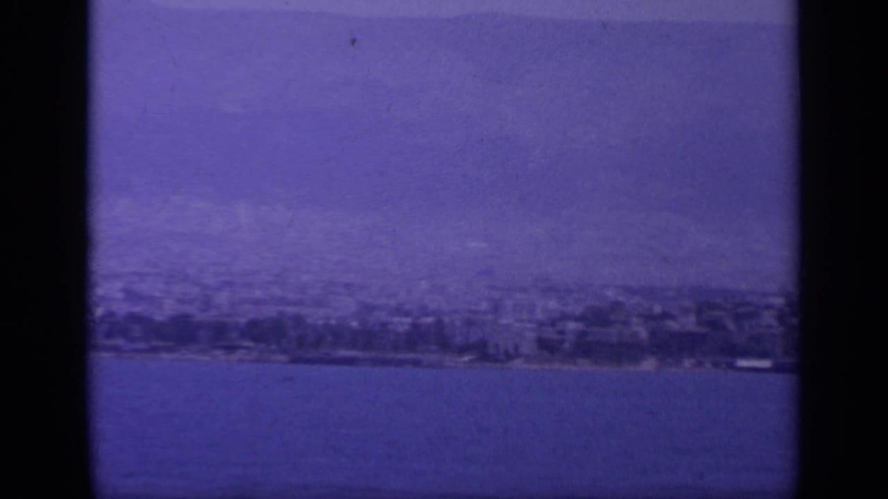 Coastal cityscape beside water with mountains fading in the background.