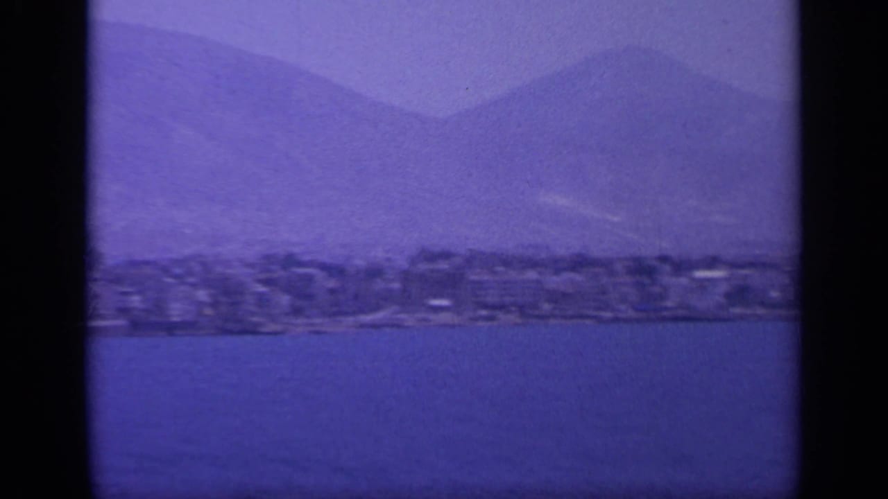 Shoreline town and mountain backdrop seen through a purple-blue film tint.