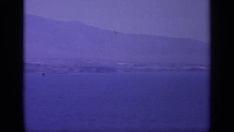 1963 Greece home-movie view of open sea, a faint distant coast, and broad mountains softened by haze and film aging.