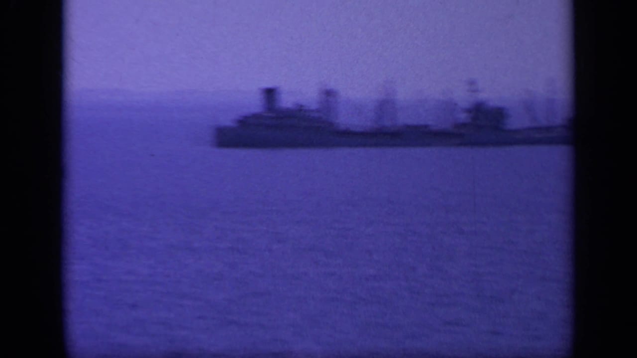 1963 Greece 8mm frame showing a large ship in silhouette on open water, with distant land behind it.