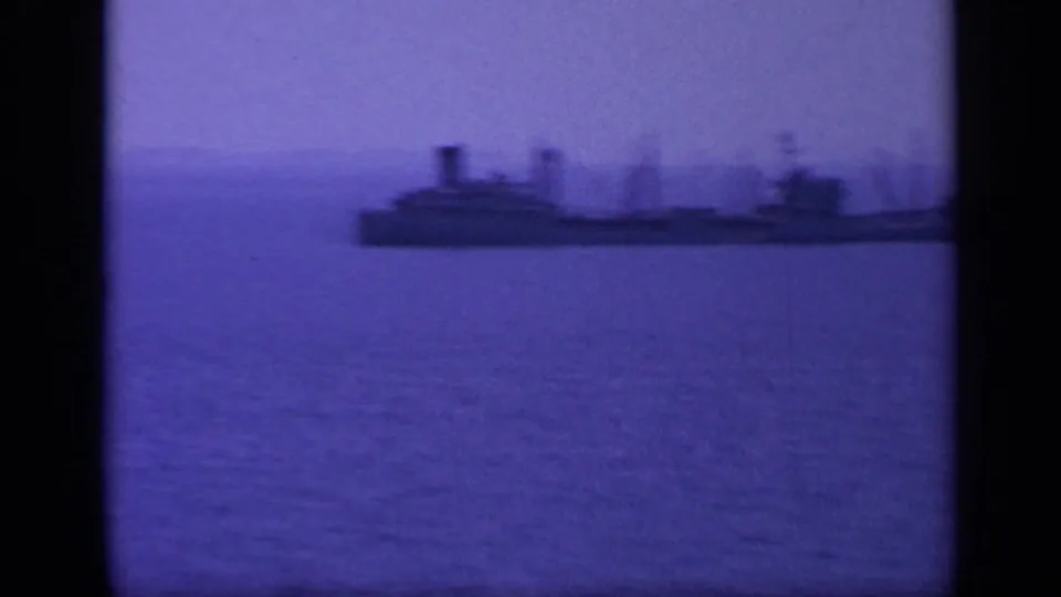 1963 Greece 8mm frame showing a large ship in silhouette on open water, with distant land behind it.