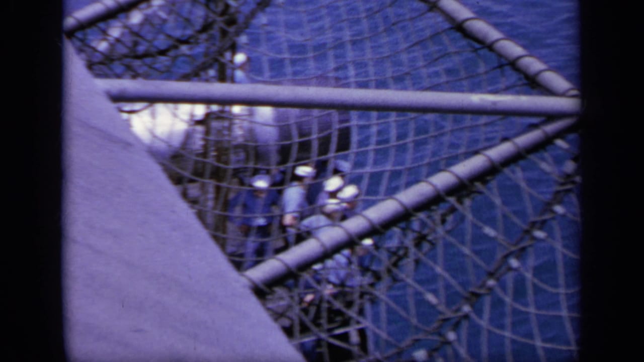 Crew members in caps on a ship deck behind rope netting and railings.