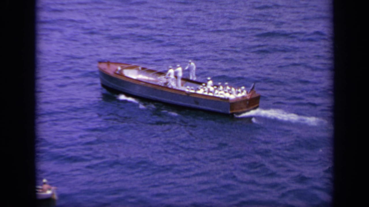 1963 Greece home-movie frame of a wooden motorboat with men in white uniforms moving across deep blue water.