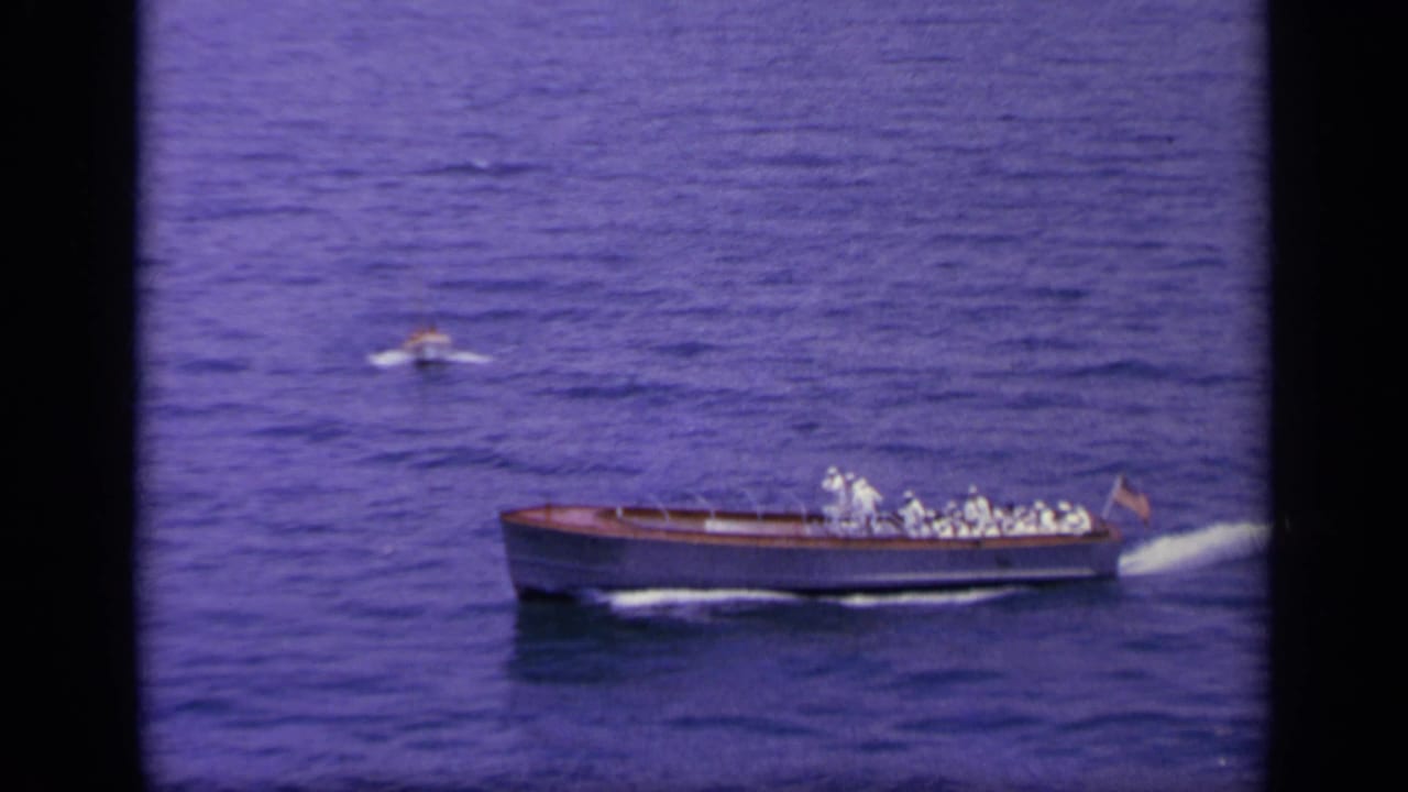 The small navy boat continues through blue water in the 1963 Greece footage, with a distant figure or small craft nearby.