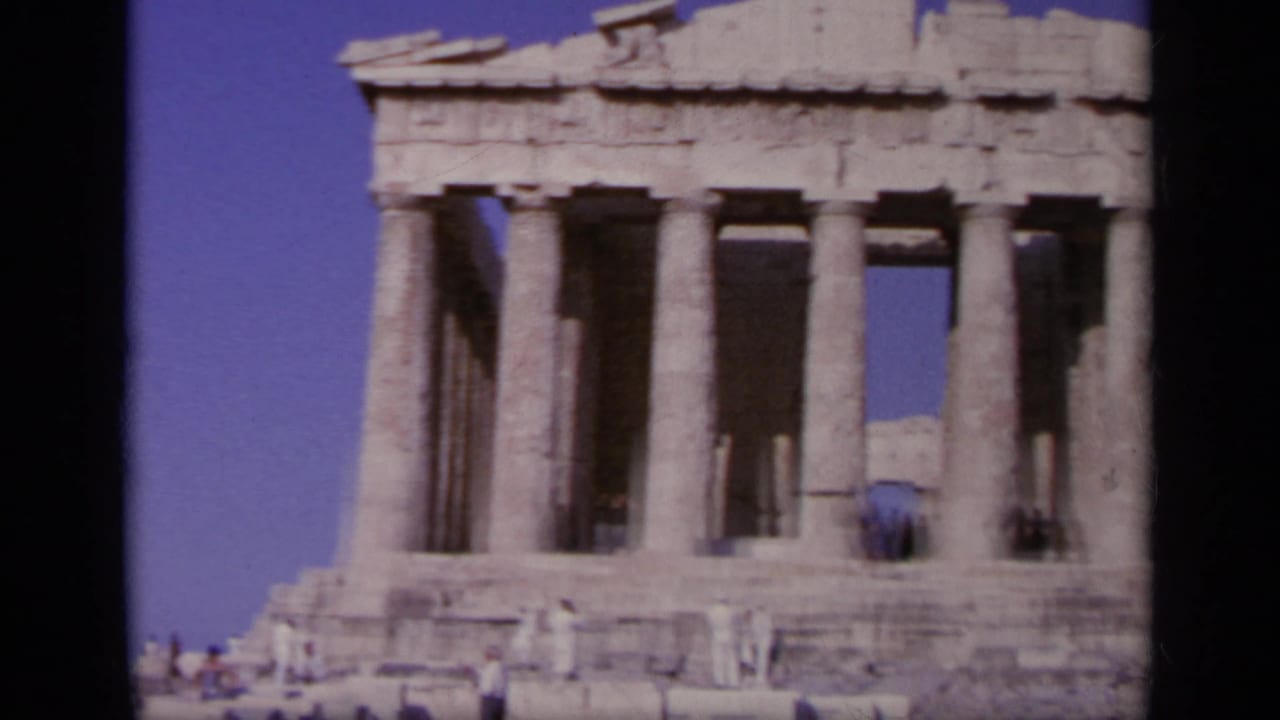 Parthenon columns and tourists standing among stone ruins under a blue sky.