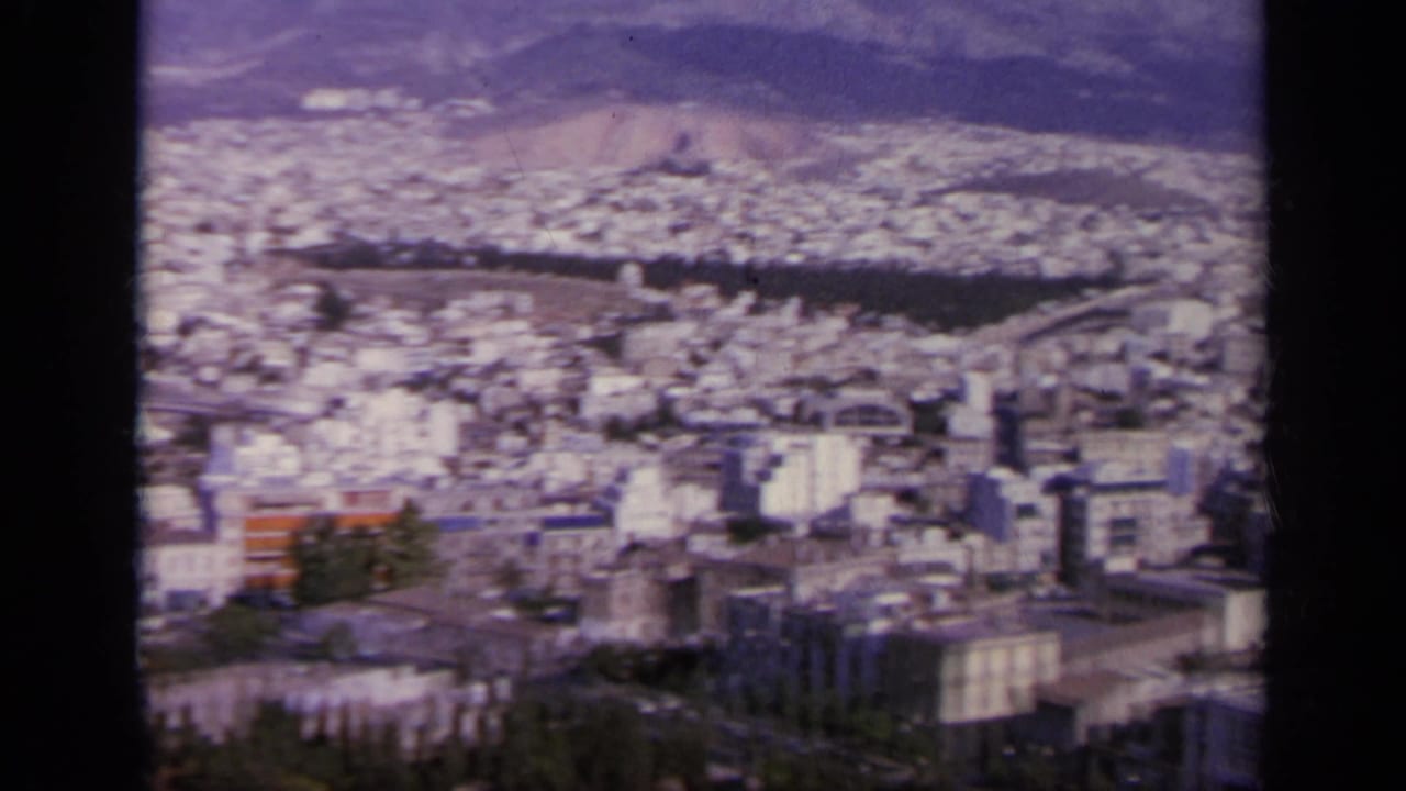 1963 Greece 8mm frame of a broad city panorama seen from a high ruin site, with mountains beyond.