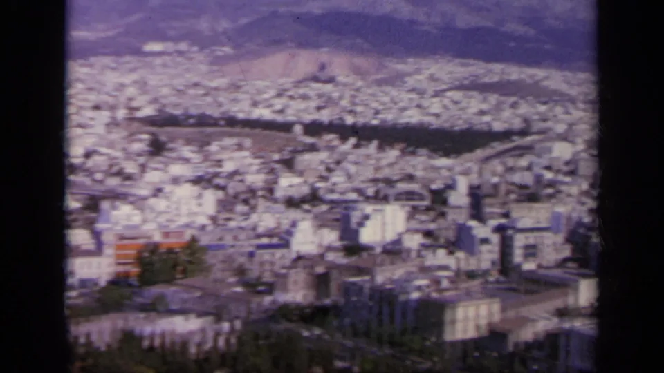 1963 Greece 8mm frame of a broad city panorama seen from a high ruin site, with mountains beyond.