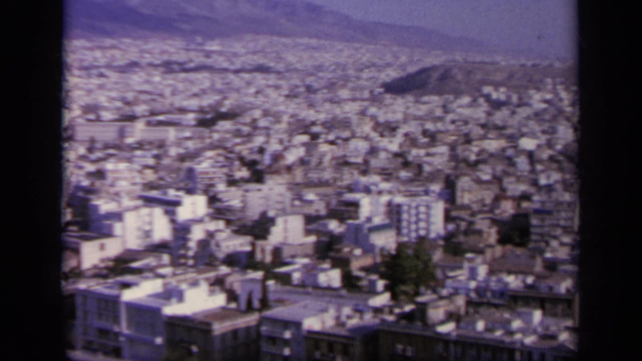 High view over a dense pale city with hills in the distance and dark film borders.