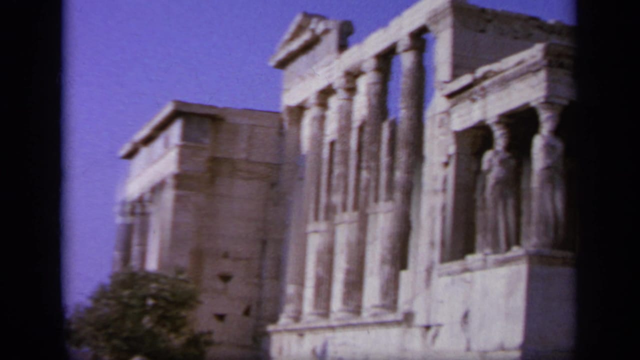 1963 Greece frame showing classical columns and carved standing figures on an ancient stone facade under a blue sky.