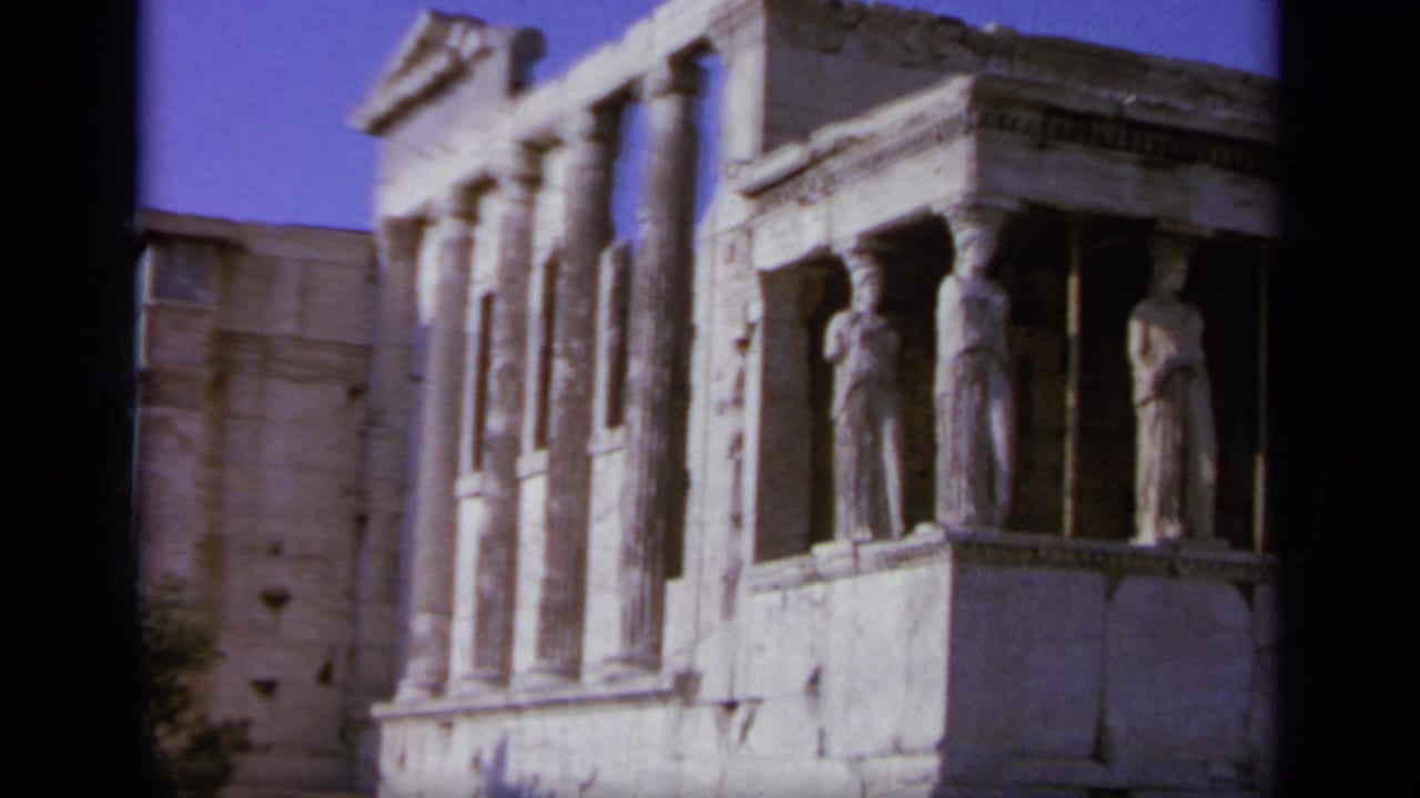 1963 Greece 8mm frame showing an ancient stone structure with caryatid figures, columns, and weathered masonry in bright sun.
