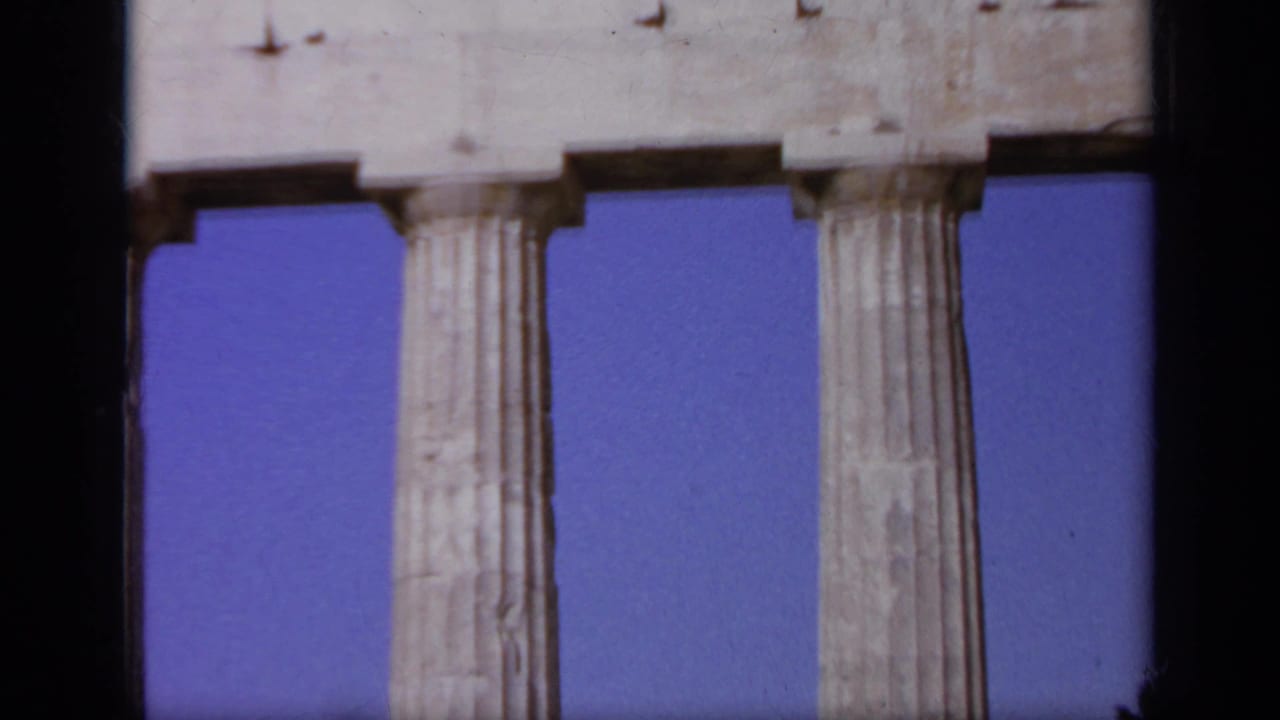 1963 Greece 8mm frame focusing on tall fluted columns and stone entablature with clear sky behind them.