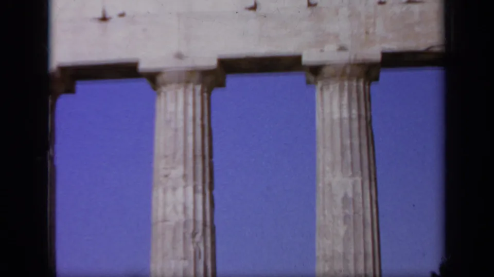 1963 Greece 8mm frame focusing on tall fluted columns and stone entablature with clear sky behind them.