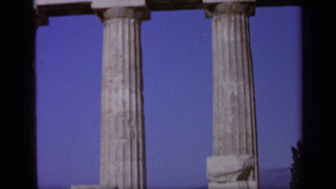 Fluted marble columns and blue sky at a Greek ruin, with figures mostly out of view.