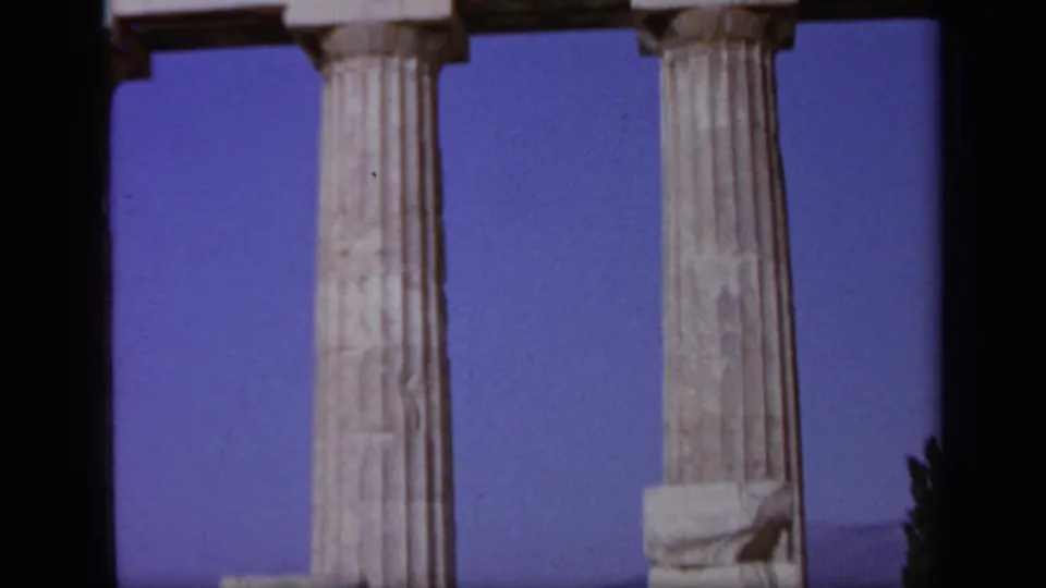 1963 Greece 8mm frame showing ancient marble columns, blue sky, and a partial visitor-shot view of a ruin site.