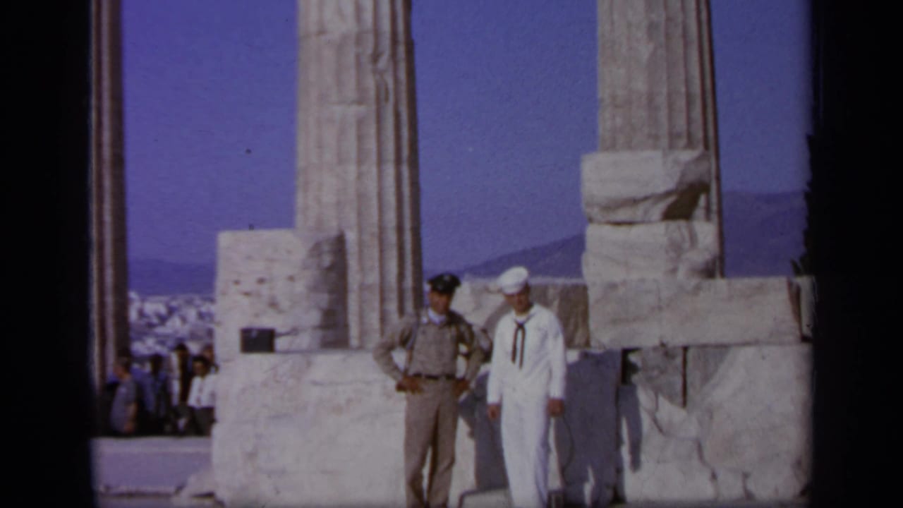 1963 Athens-area home-movie frame of a U.S. Navy sailor and tan-uniformed official posing among ancient marble columns.