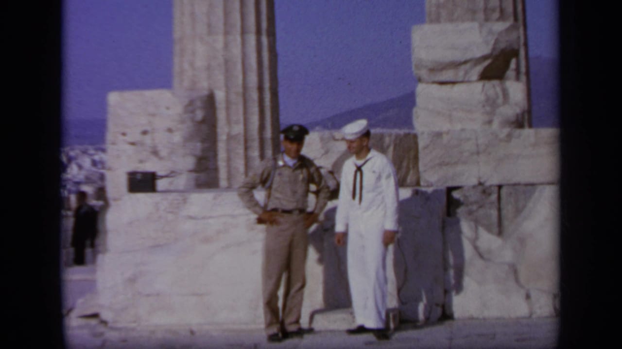 1963 Greece 8mm frame showing a sailor in white and a tan-uniformed official posing at an ancient marble site.