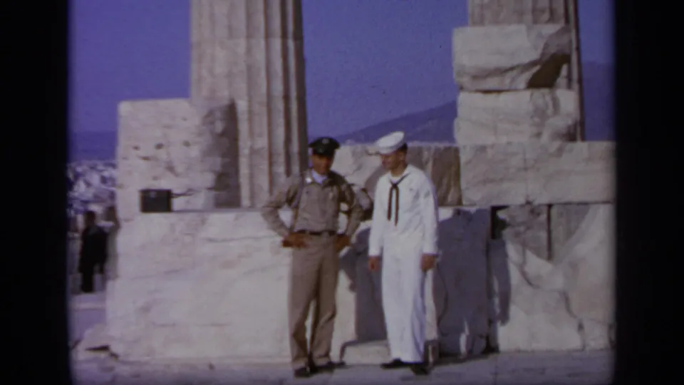 1963 Greece 8mm frame showing a sailor in white and a tan-uniformed official posing at an ancient marble site.