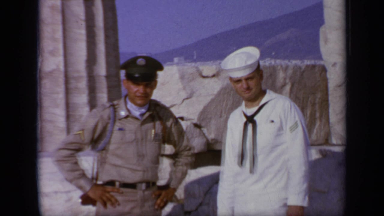 A tan-uniformed officer and a sailor in white stand near stone ruins.