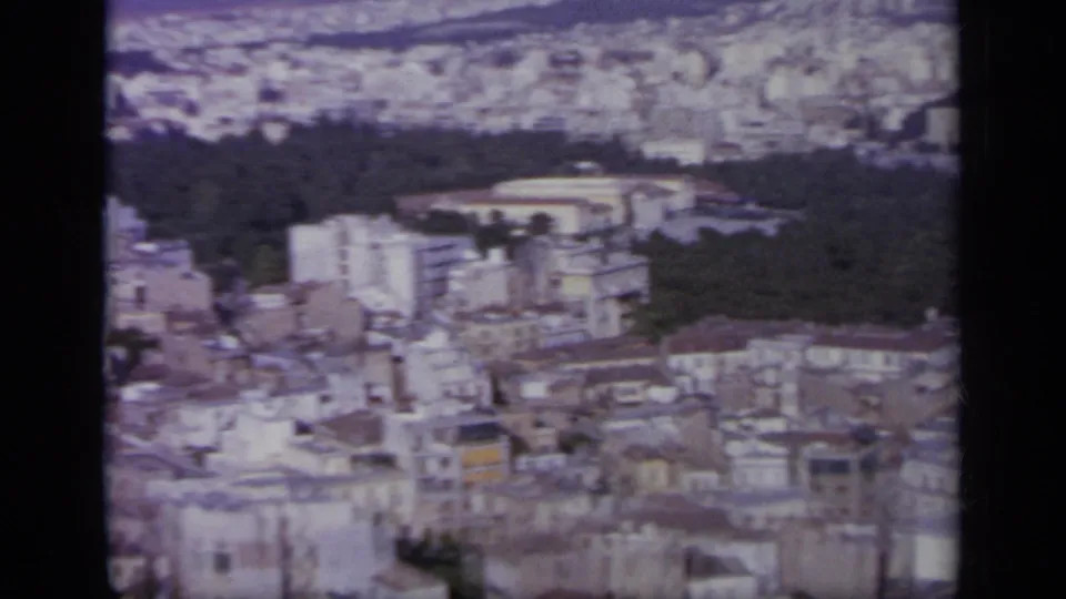 1963 Greece frame showing a high city view with a wooded area, oval stadium-like landmark, and surrounding buildings.