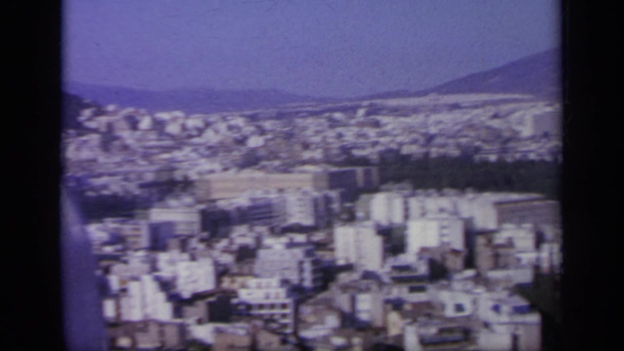 1963 Greek city panorama with white buildings, distant hills, and a dark mountain slope beyond the urban area.