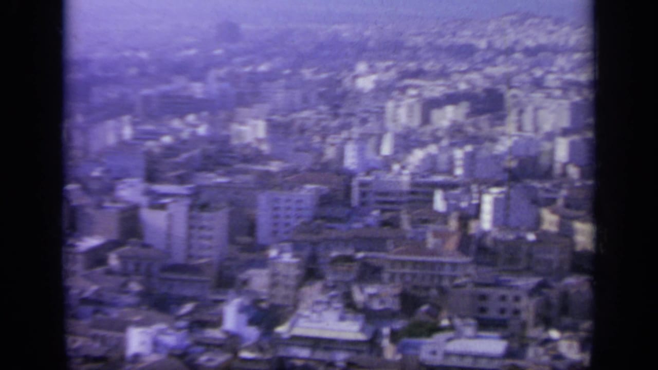 Dense hillside cityscape with pale buildings under a hazy sky.