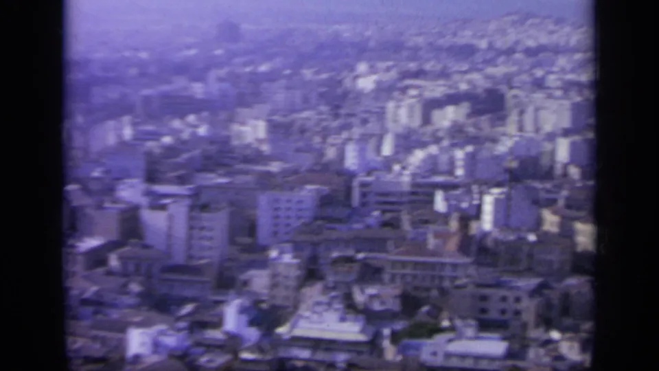 1963 Greece 8mm frame showing a dense hillside cityscape with pale apartment blocks and older buildings in haze.