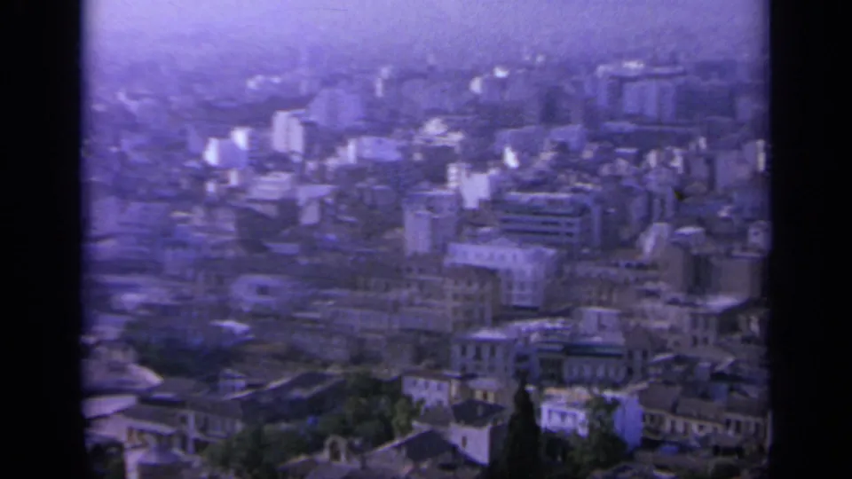 1963 Greece 8mm view across a dense urban district with apartment blocks, older roofs, and distant haze.