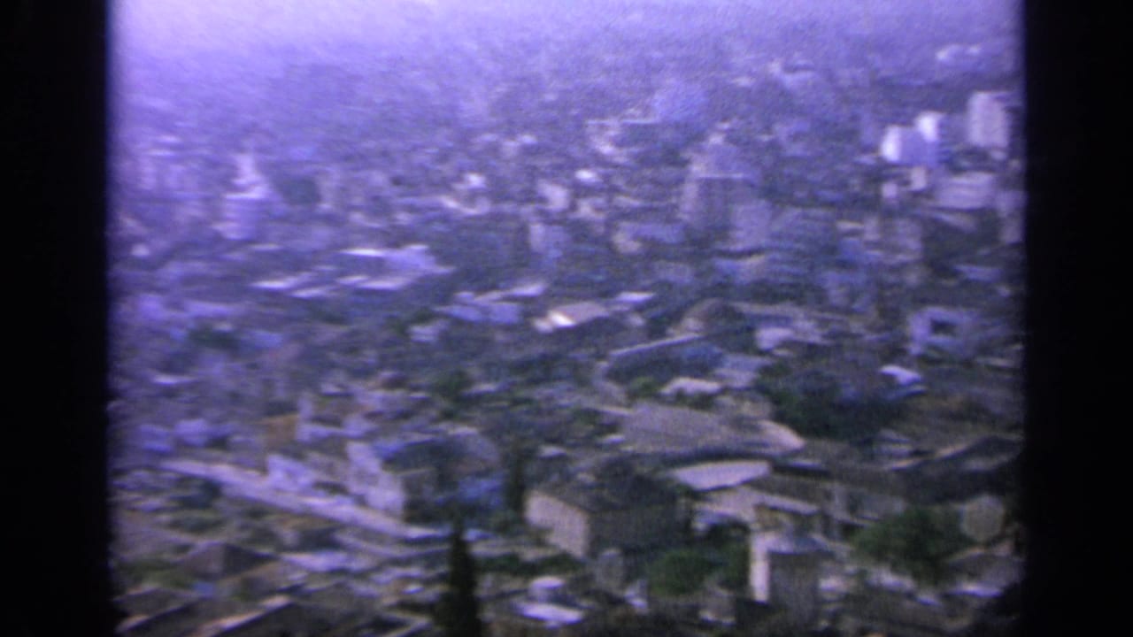 1963 Greece 8mm frame with a soft hazy city view, low rooftops, taller blocks, and scattered trees.