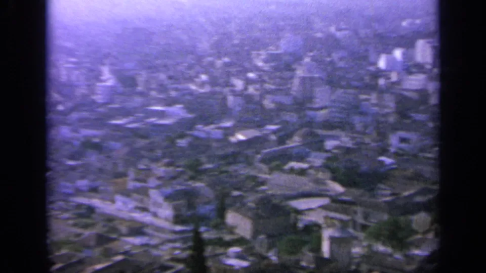 1963 Greece 8mm frame with a soft hazy city view, low rooftops, taller blocks, and scattered trees.