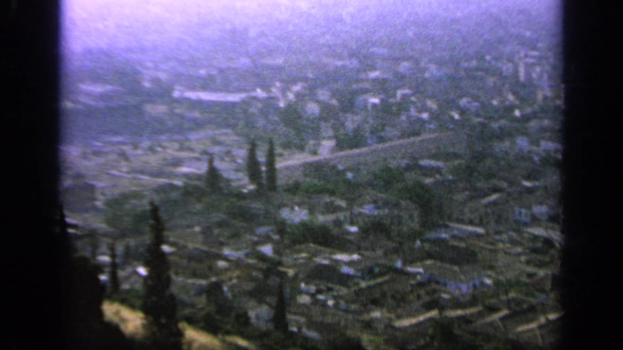 Hazy elevated view over a Greek city with trees and dark film borders.