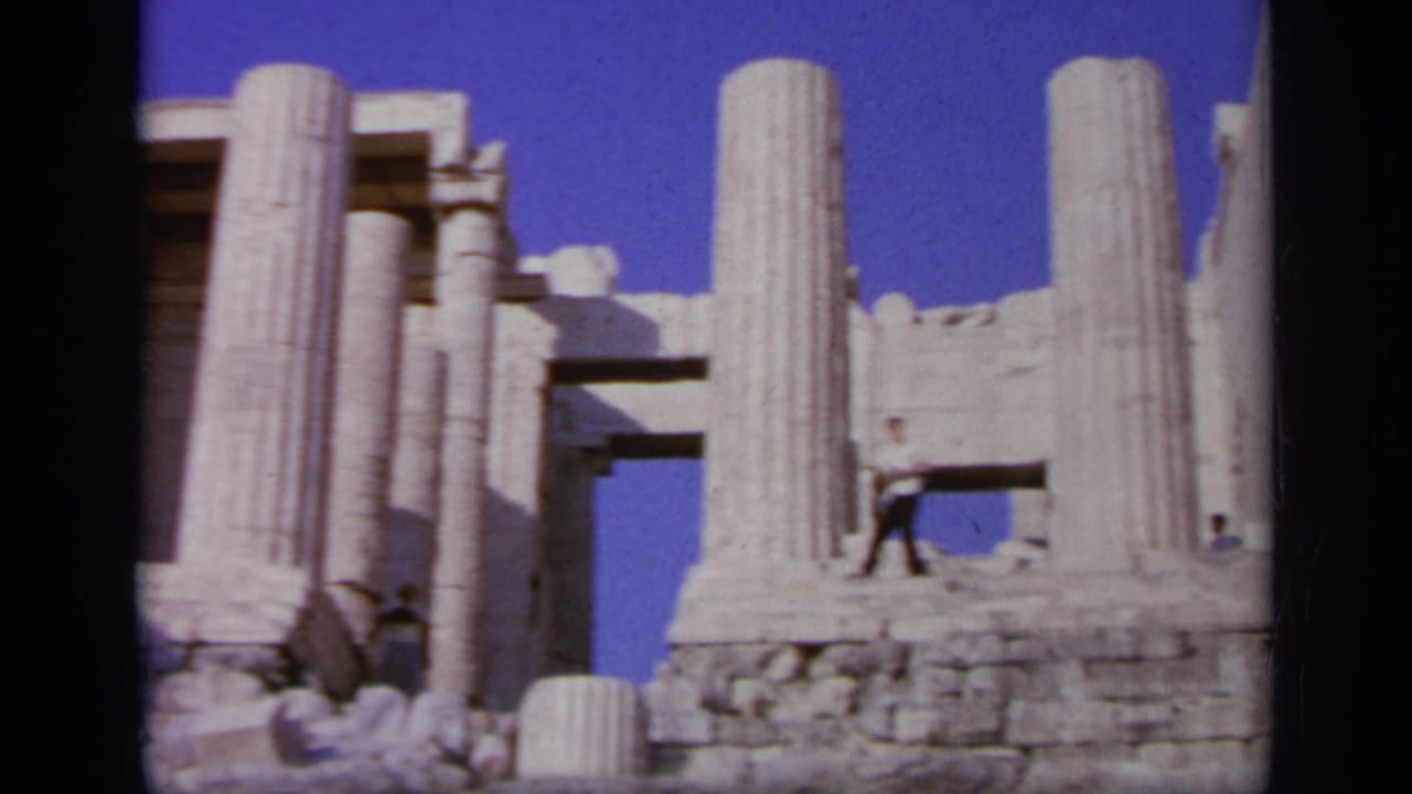 1963 Greece travel frame with classical stone columns, weathered blocks, and a distant tourist among the ruins.