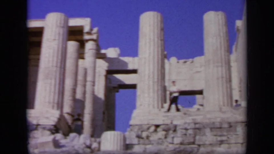 1963 Greece travel frame with classical stone columns, weathered blocks, and a distant tourist among the ruins.