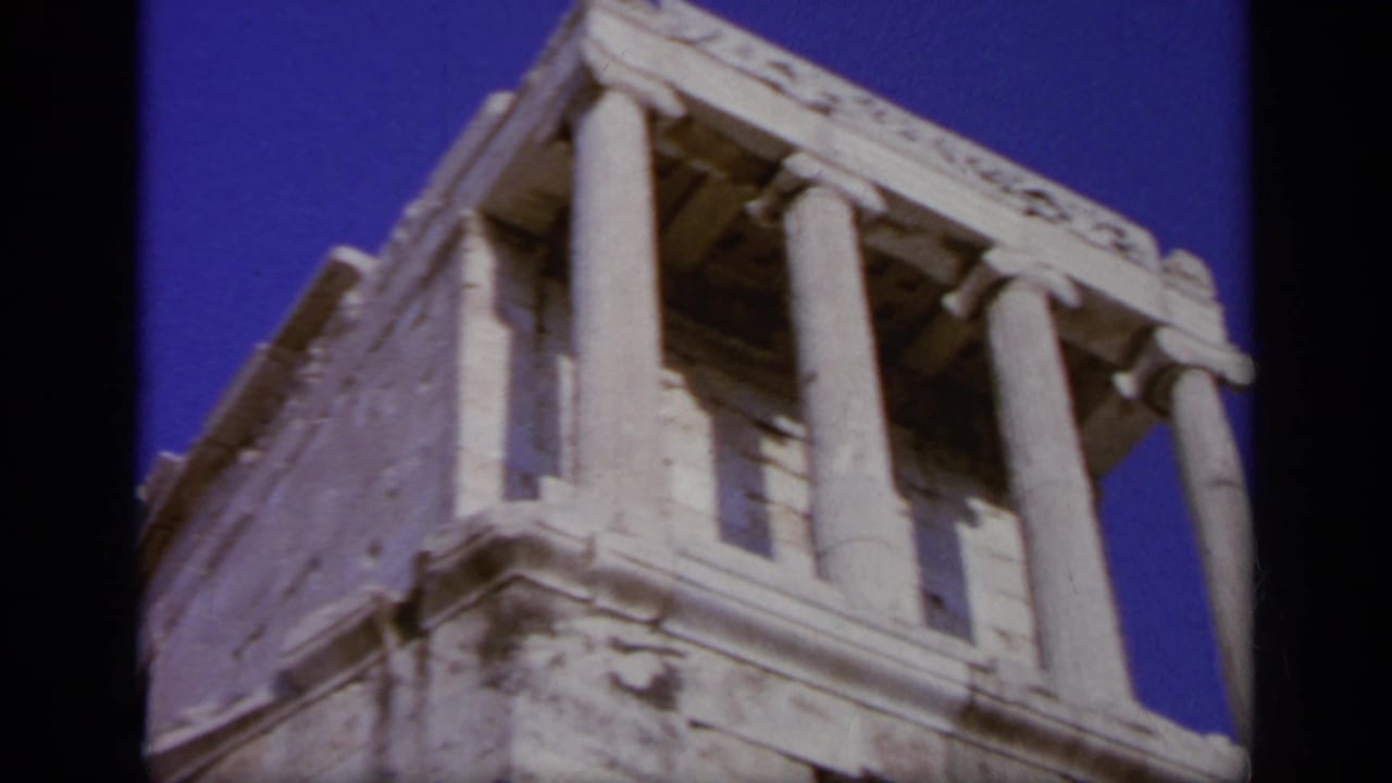 1963 Greece home-movie frame showing a classical stone structure with columns, filmed from a low angle under bright blue sky.