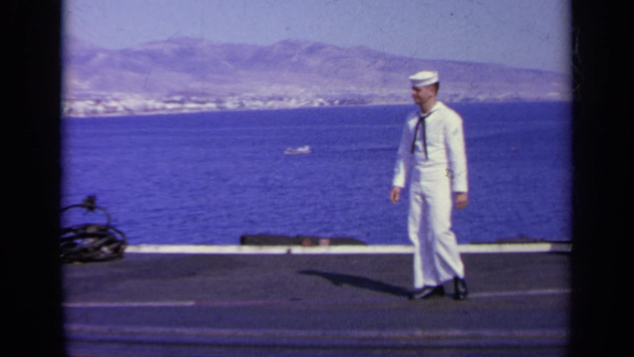 1963 Greece 8mm frame showing a sailor in white uniform on a ship deck above blue water and a distant coastal town.