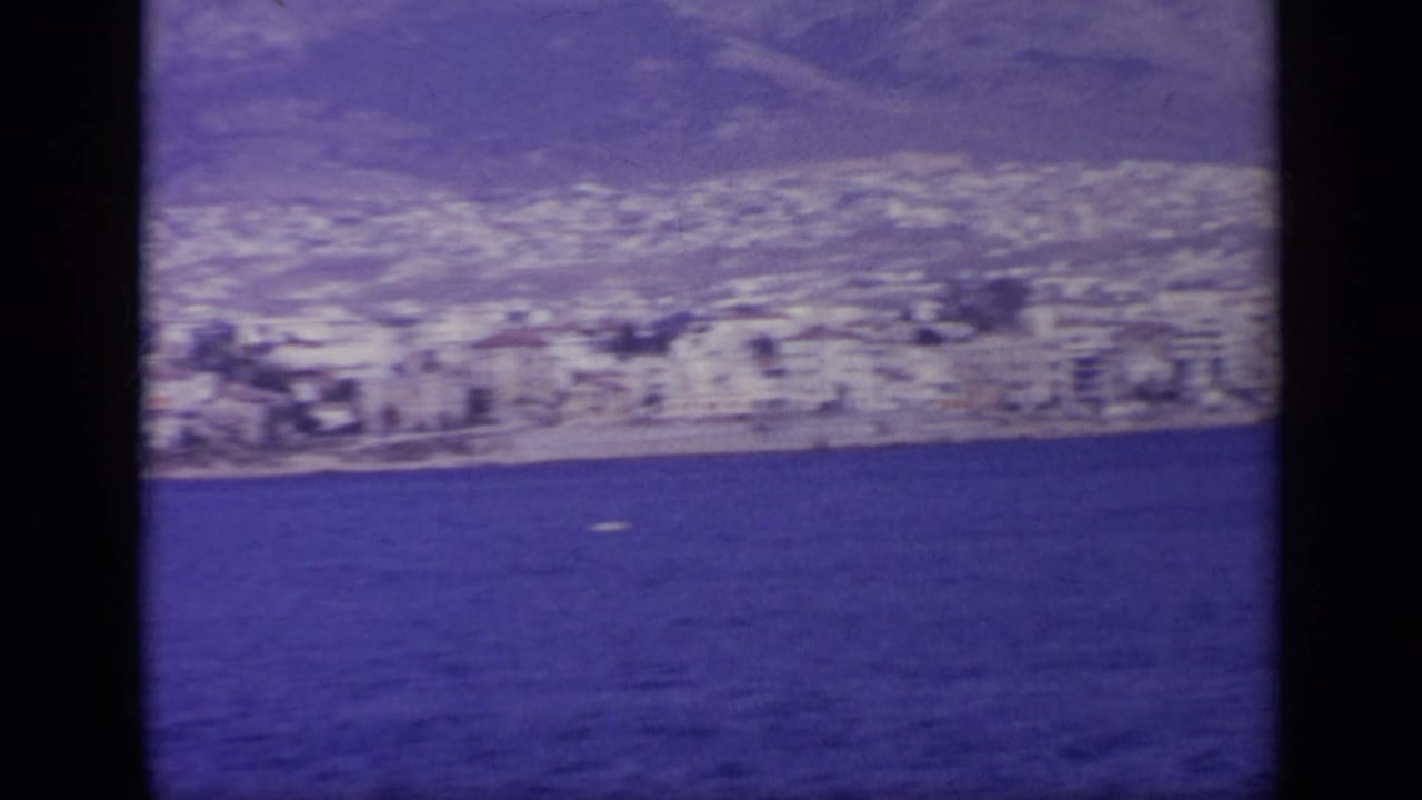 Coastal town with white buildings along a shoreline seen across blue water.
