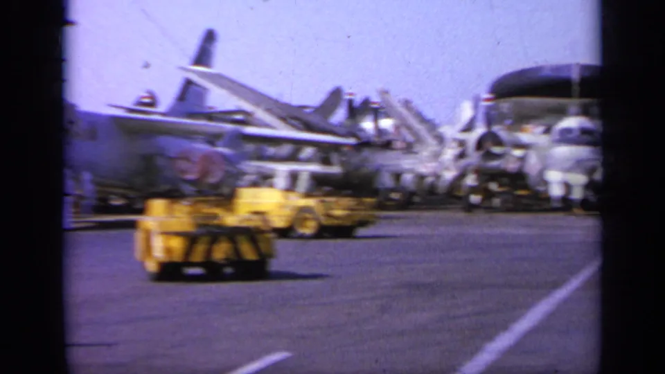 Parked naval aircraft and yellow ground support equipment appear on an aircraft carrier deck in 1963 Greece footage.