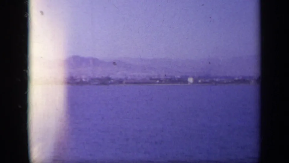 1963 Greece 8mm frame showing open water, a faint distant shoreline, hazy mountains, and a vertical light leak.