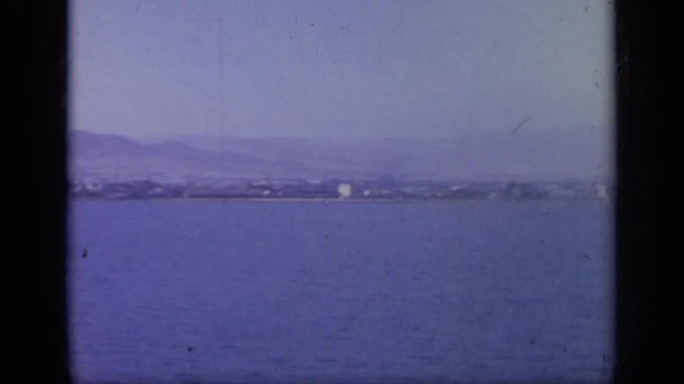 1963 Greece 8mm frame showing open water, a faint coastal skyline and mountains through haze and film grain.